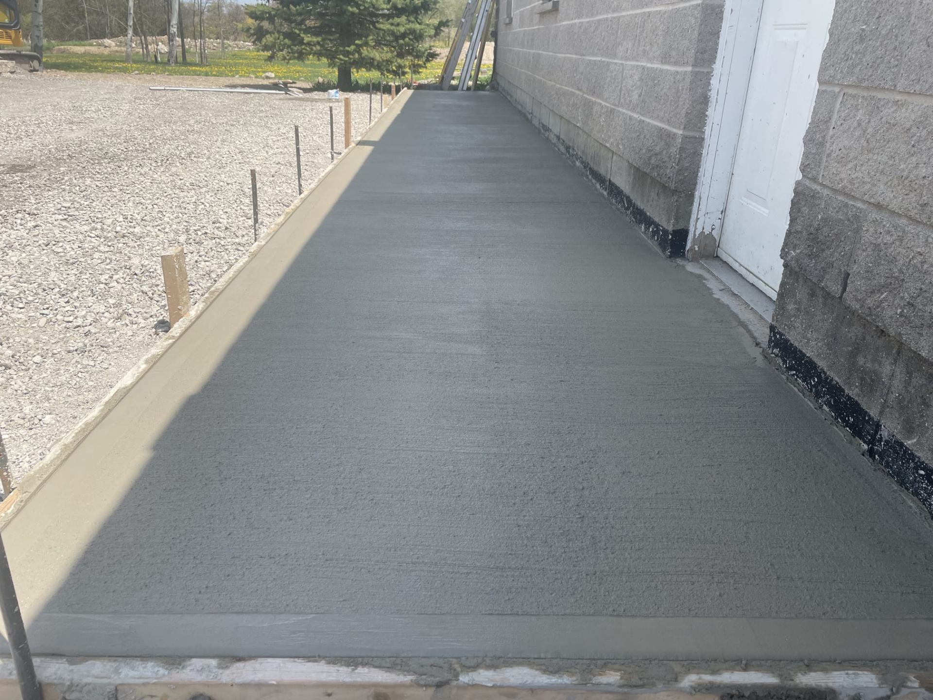 Freshly finished broom-textured concrete sidewalk beside a block foundation