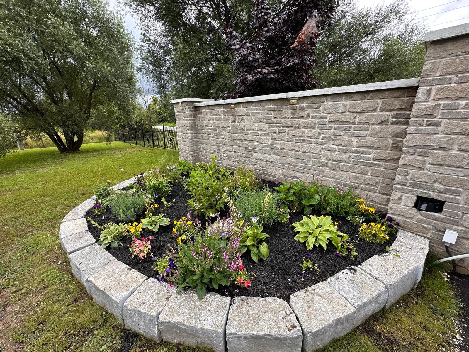 Curved garden bed with natural stone edging in front of a cut-stone wall